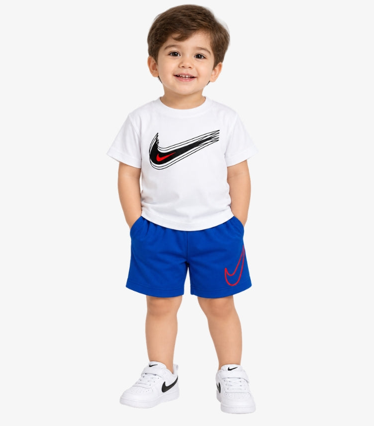 Baby boy wearing Nike white short-sleeve T-shirt with black and red Swoosh graphic, royal blue shorts with red Nike logo and white sneakers.