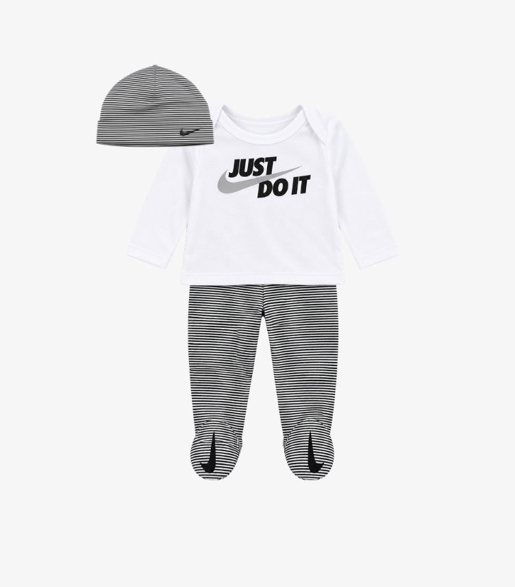 Nike baby 3-piece outfit set featuring white long sleeve Just Do It graphic top, black and white striped footed pants and matching striped beanie hat.