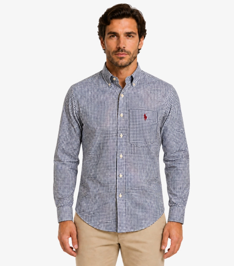 Male model wearing a U.S. Polo Assn. men’s navy blue and white gingham-check long-sleeve shirt with chest pocket and embroidered red logo