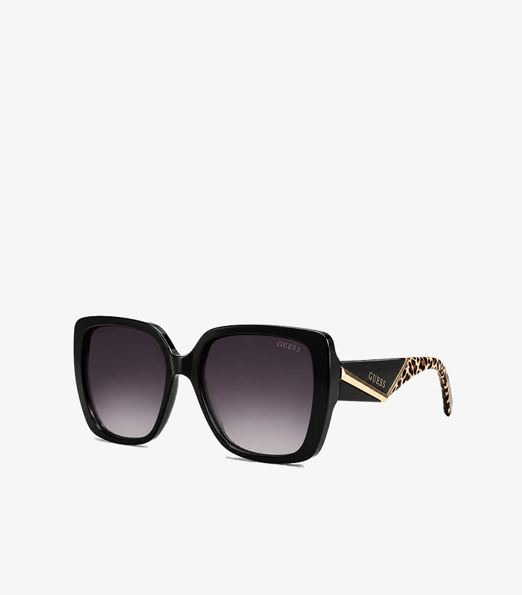 Guess women's oversized square sunglasses with gradient UV protection lenses, glossy frame, signature logo, and animal-print temple detailing, angled view.