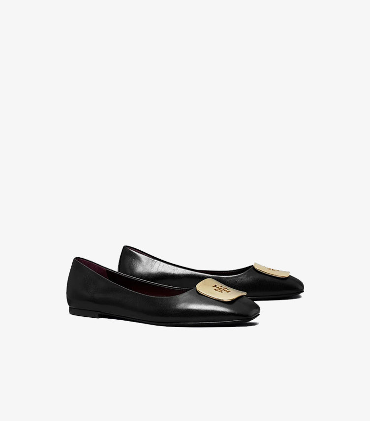 Angled view of Tory Burch black ballet flats featuring gold-tone logo plaques and low-profile soles
