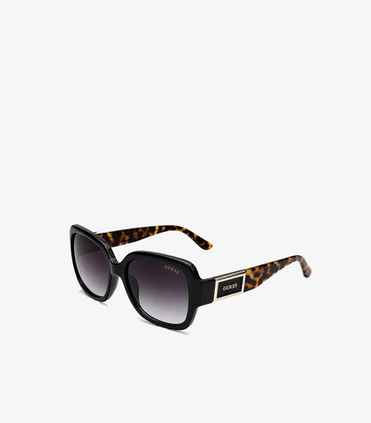 Angled view of Guess women’s black oversized square sunglasses with gradient lenses, tortoiseshell arms and gold logo plaques
