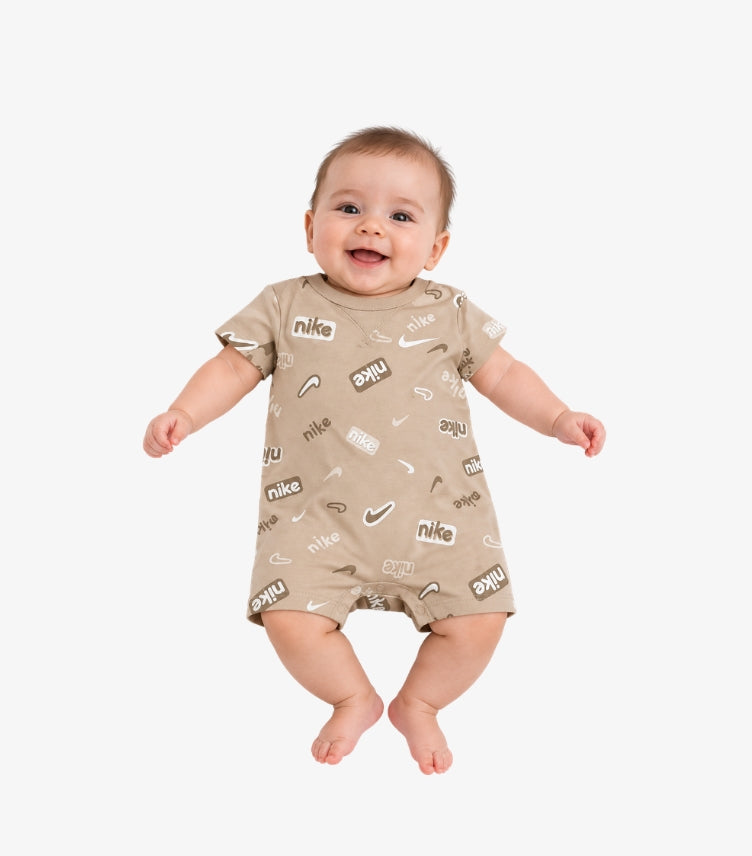 Baby wearing a beige Nike short-sleeve romper with an all-over wordmark and Swoosh logo print