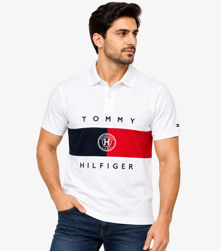 Man wearing a Tommy Hilfiger white short-sleeve polo shirt with navy and red colour-block panels, logo lettering, chest crest and sleeve flag