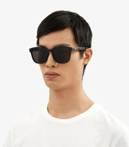 Male model wearing Gucci men’s black square-frame sunglasses with dark lenses and gold-tone GG temple logos