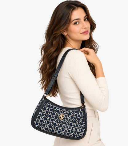 Woman carrying a Tommy Hilfiger navy and cream monogram shoulder bag with adjustable strap and gold-tone TH logo