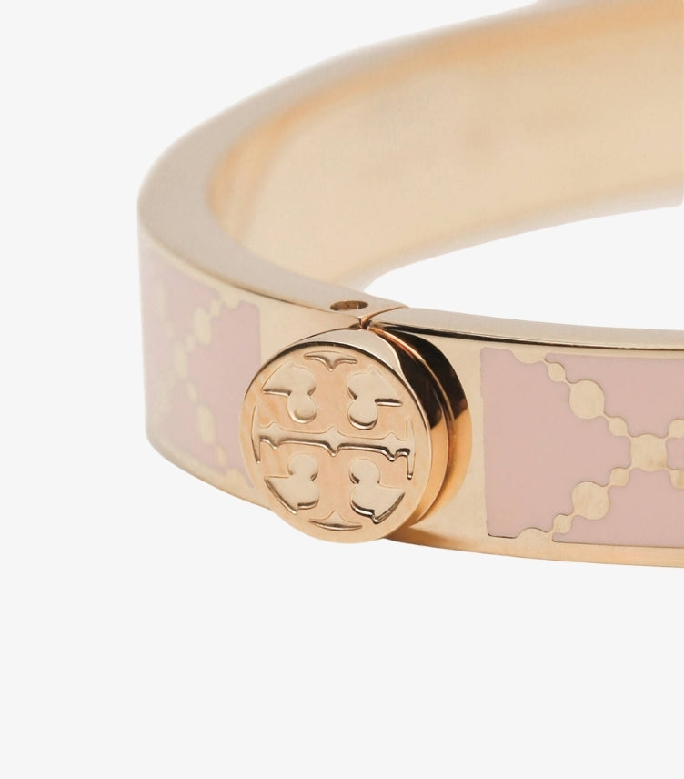 Close-up of Tory Burch blush-pink enamel bangle showing circular Double T logo and polished gold-tone finish