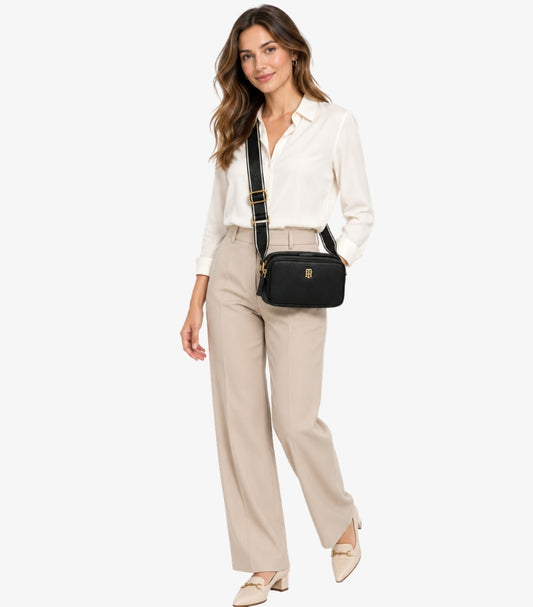 Woman wearing a Tommy Hilfiger double-zip camera bag with a wide branded adjustable crossbody strap