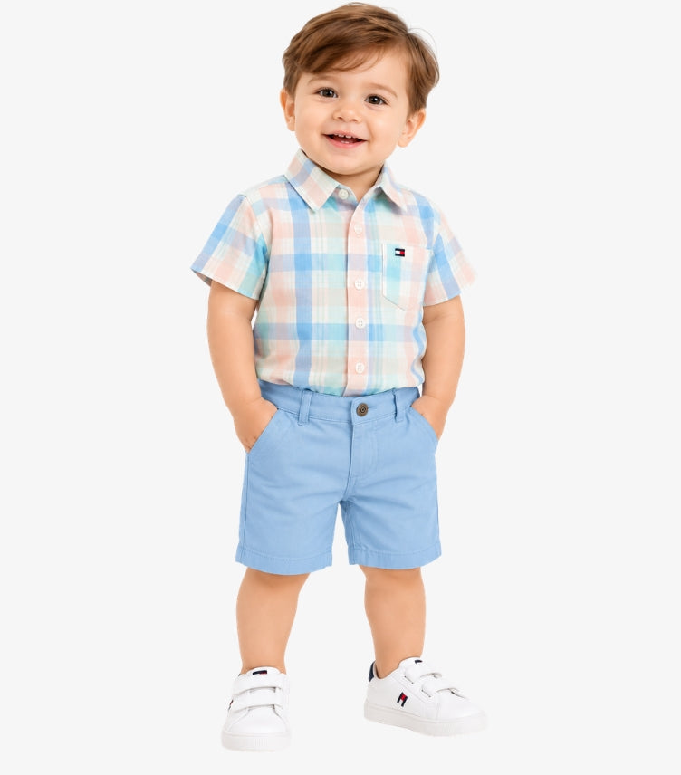 Tommy Hilfiger baby boy wearing a pastel checked short-sleeve shirt with light blue shorts, featuring signature flag logo details.