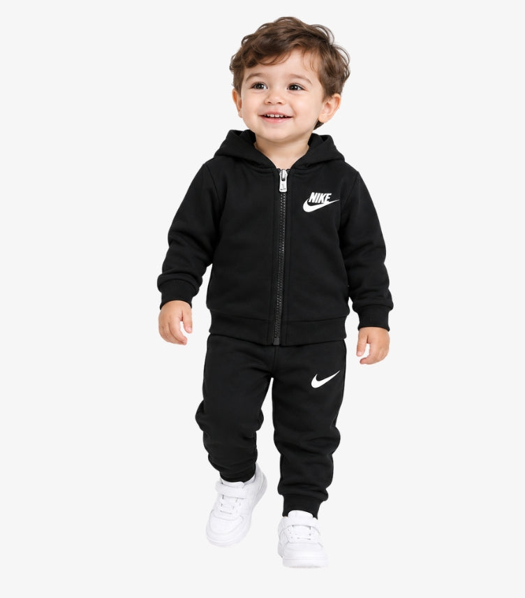 Baby boy wearing Nike zip-up hooded jacket and matching jogger pants featuring Nike Swoosh branding and ribbed cuffs.