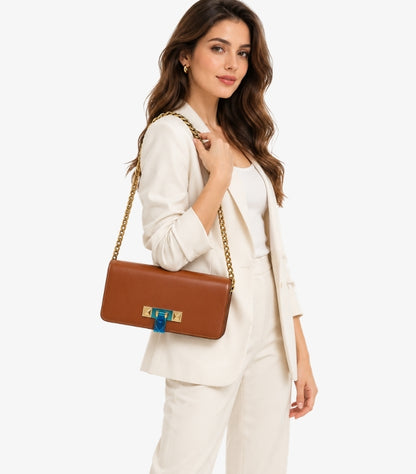 Model holding a Valentino brown flap bag close up, showing its chain strap, tonal stitching and gold-tone hardware