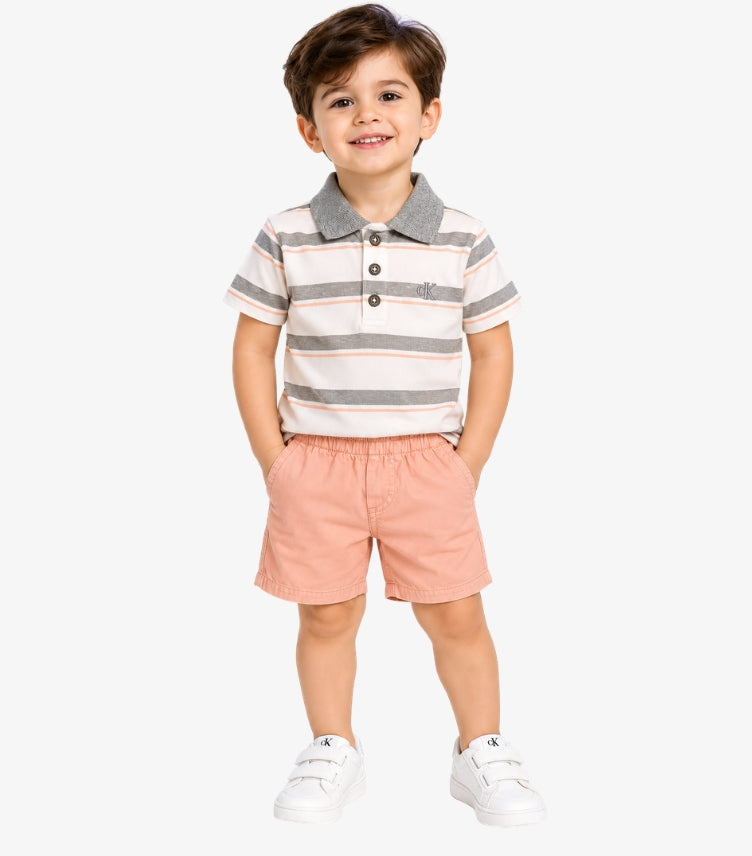 Boy wearing a Calvin Klein striped short-sleeve polo shirt with peach elasticated shorts and white trainers