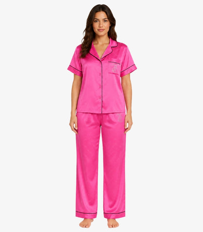 Juicy Couture women's pink satin pajama set with short sleeve button-up shirt, matching full-length pants, rhinestone logo, and contrast piping front view.
