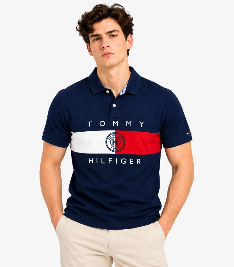 Man wearing a Tommy Hilfiger navy short-sleeve polo shirt with red and white colour-block panels, logo lettering and chest crest