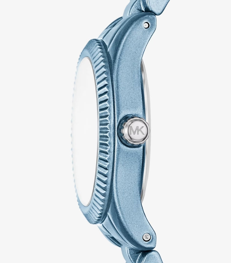 Close-up side view of Michael Kors blue-tone watch showing its fluted bezel and silver MK logo crown