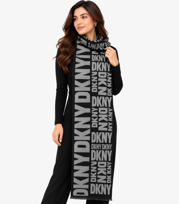 DKNY Women's Black and Grey Logo Print Shawl featuring bold oversized DKNY lettering, contrasting black border and fringed edges, styled on a female model.