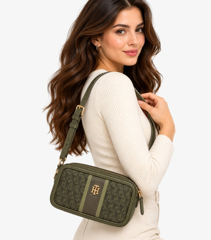 Woman carrying a Tommy Hilfiger olive monogram crossbody camera bag with adjustable strap and gold-tone TH logo