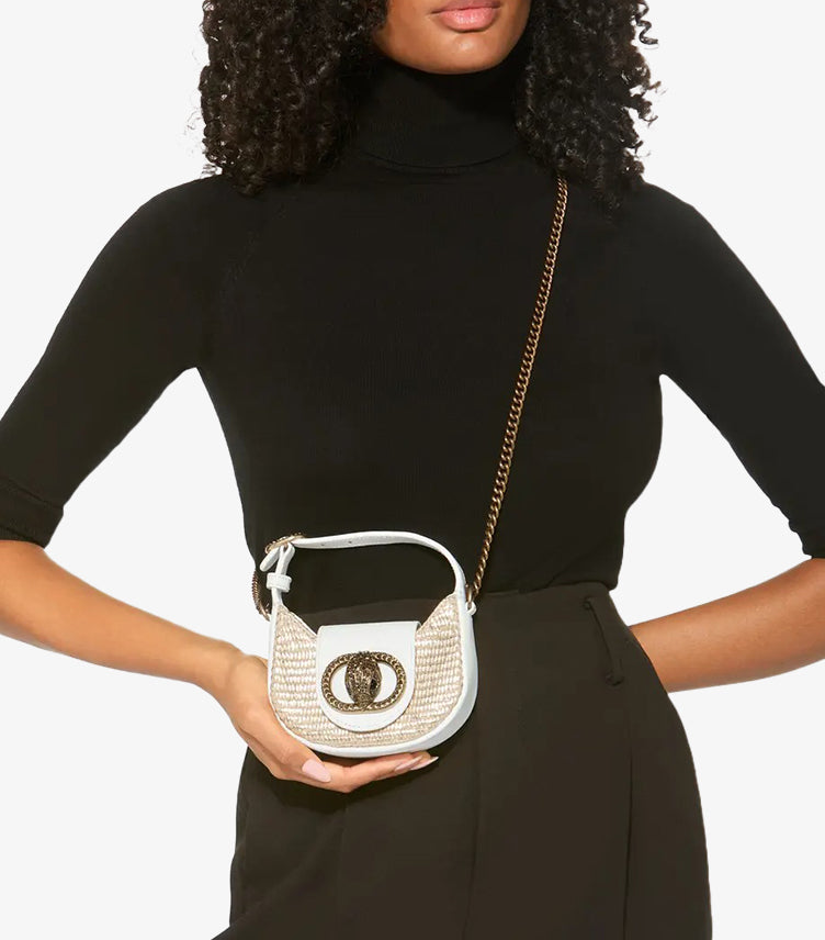 Woman carrying Kurt Geiger Micro Chelsea beige rattan crossbody bag with antique brass chain