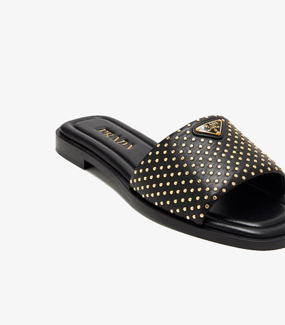 Prada black studded leather flat slide sandal angled close-up showing gold triangle logo plaque and allover micro-studs