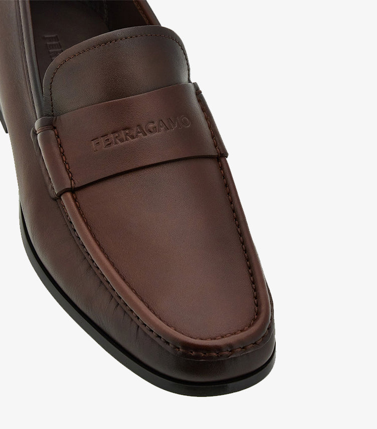 Close-up of Ferragamo brown leather penny loafer with embossed logo and apron-toe stitching