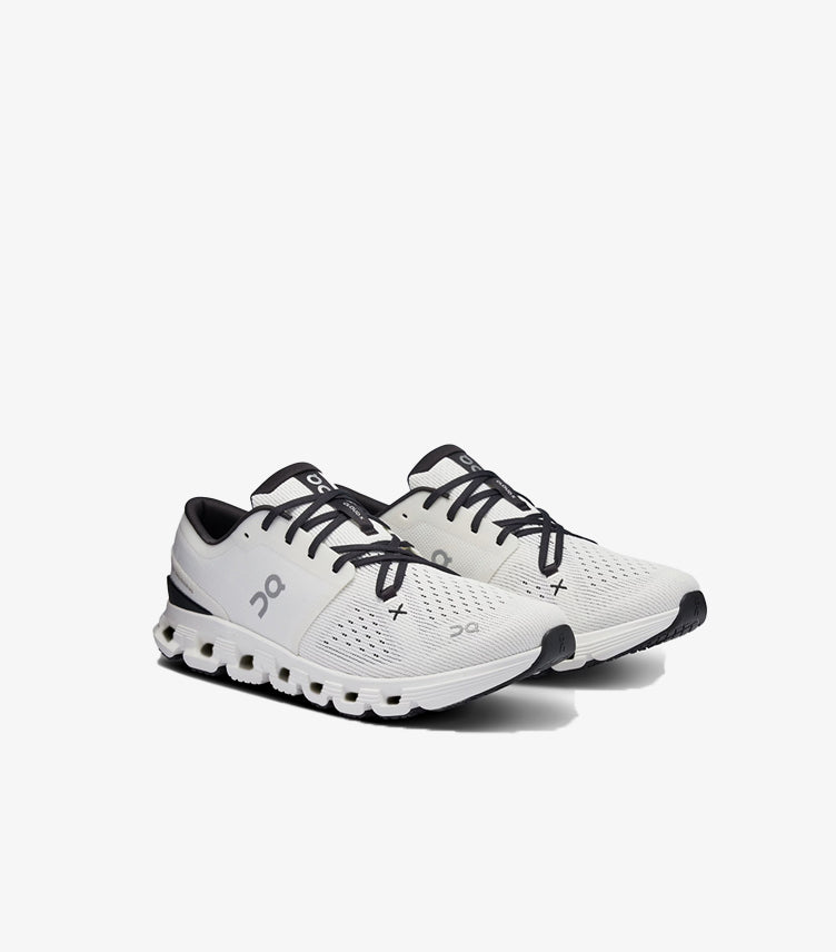 Angled view of On Running Cloud X white and black training shoes with mesh uppers and cloud-element soles