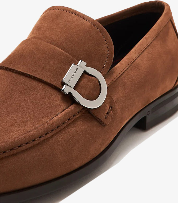 Close-up of Ferragamo brown suede loafer showing engraved silver-tone Gancini ornament and tonal stitching