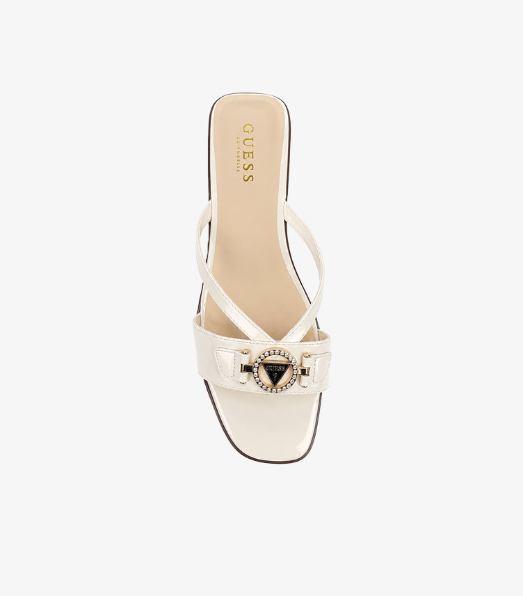 GUESS cream patent leather slides top-down view showing asymmetric cross-straps crystal triangle medallion and GUESS LOS ANGELES branded insole