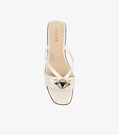 GUESS cream patent leather slides top-down view showing asymmetric cross-straps crystal triangle medallion and GUESS LOS ANGELES branded insole