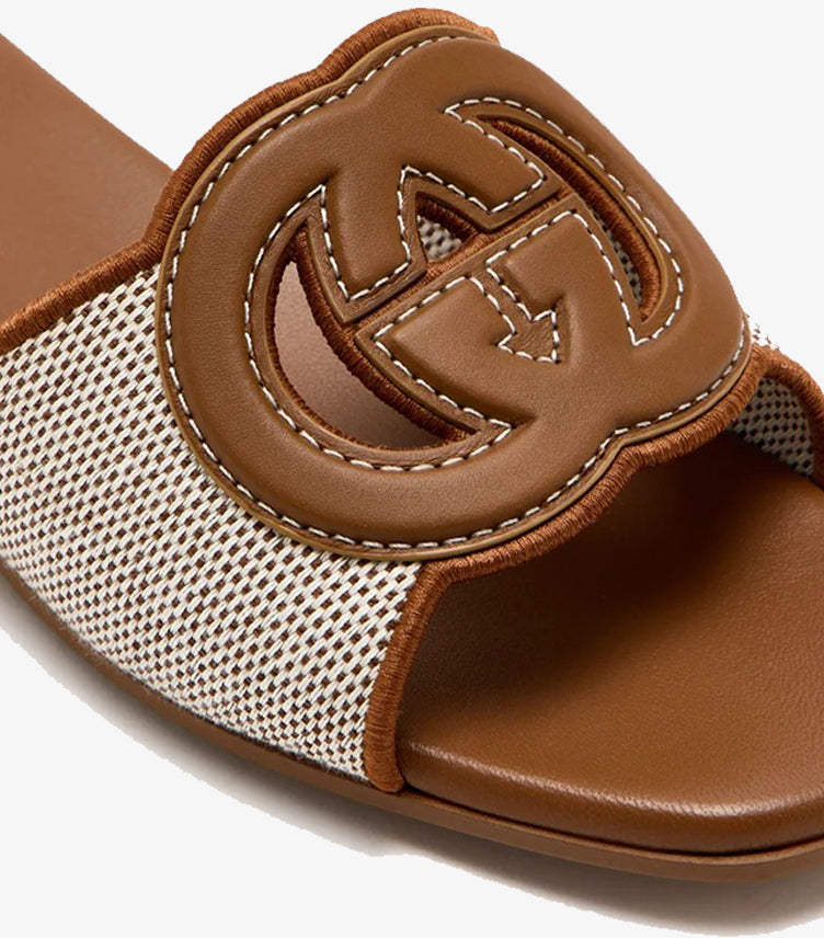 Close-up of Gucci Interlocking GG cutout logo in tan leather with white contrast stitching on cream canvas slide