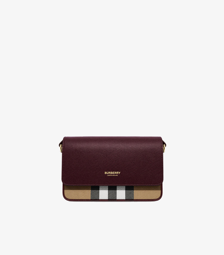 Front view of Burberry women’s burgundy flap crossbody bag with signature beige check panel and gold-tone logo