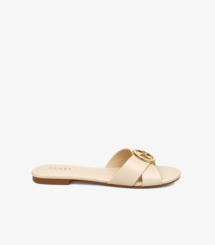 Side view of Guess cream slip-on sandal with crossover upper, circular logo hardware and slim flat sole